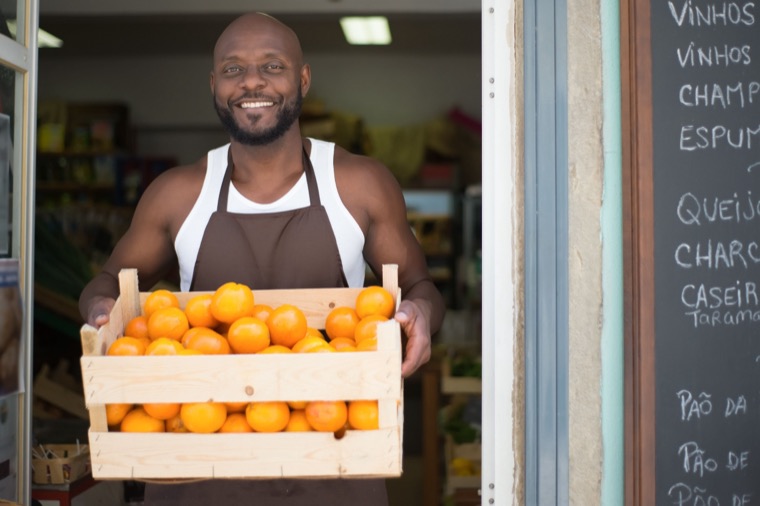 A shopkeeper holding a crate of oranges in his store